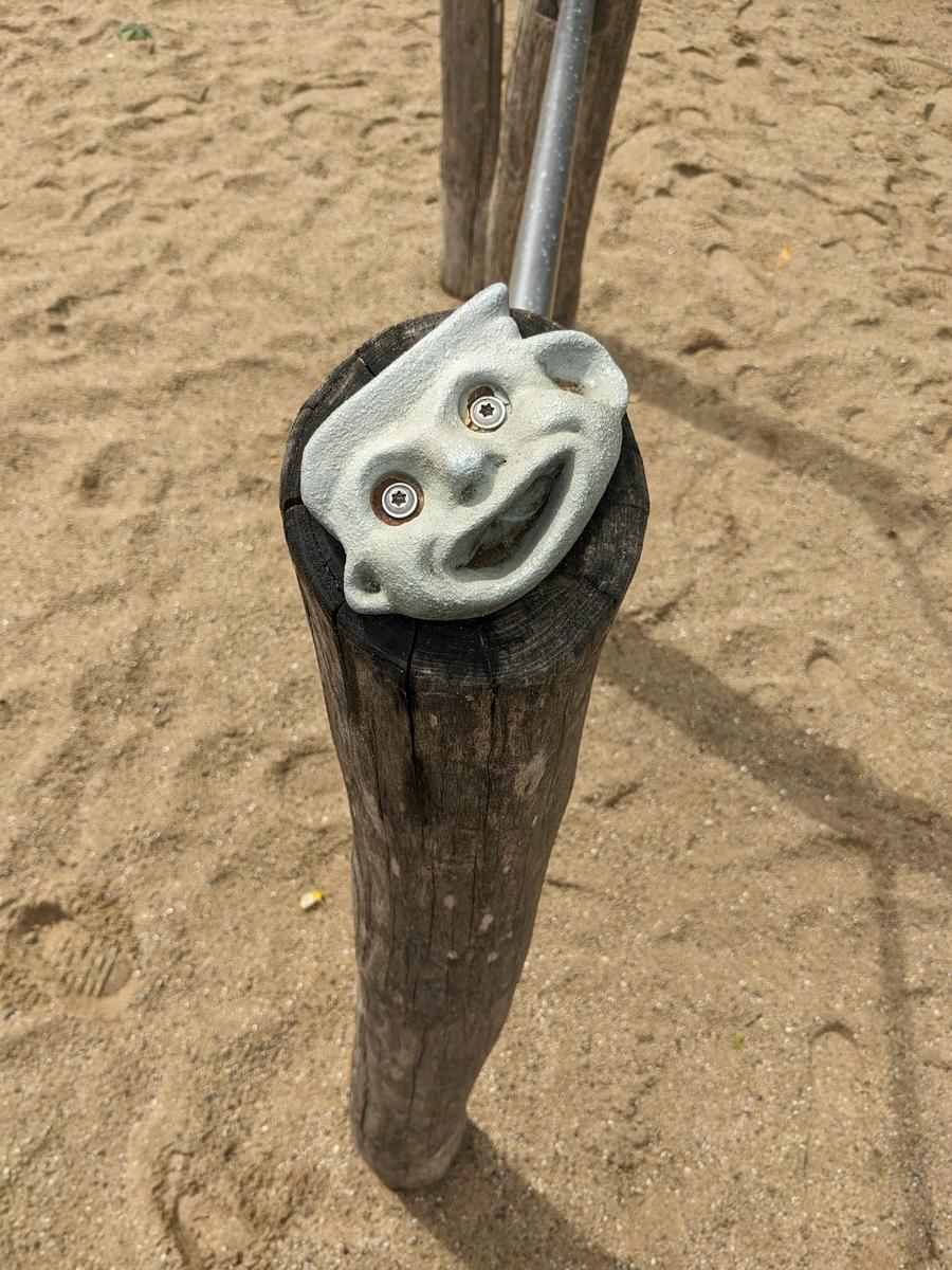 A strange grimacing face on top of a wooden pole, in a kids playground.