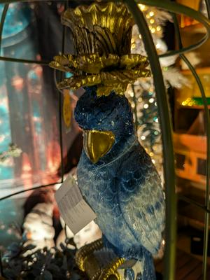 A decorative blue Phoenix figure with a golden beak and a golden, crown-like headpiece, 
                    positioned inside a cage, with soft, out-of-focus lights in the background.
