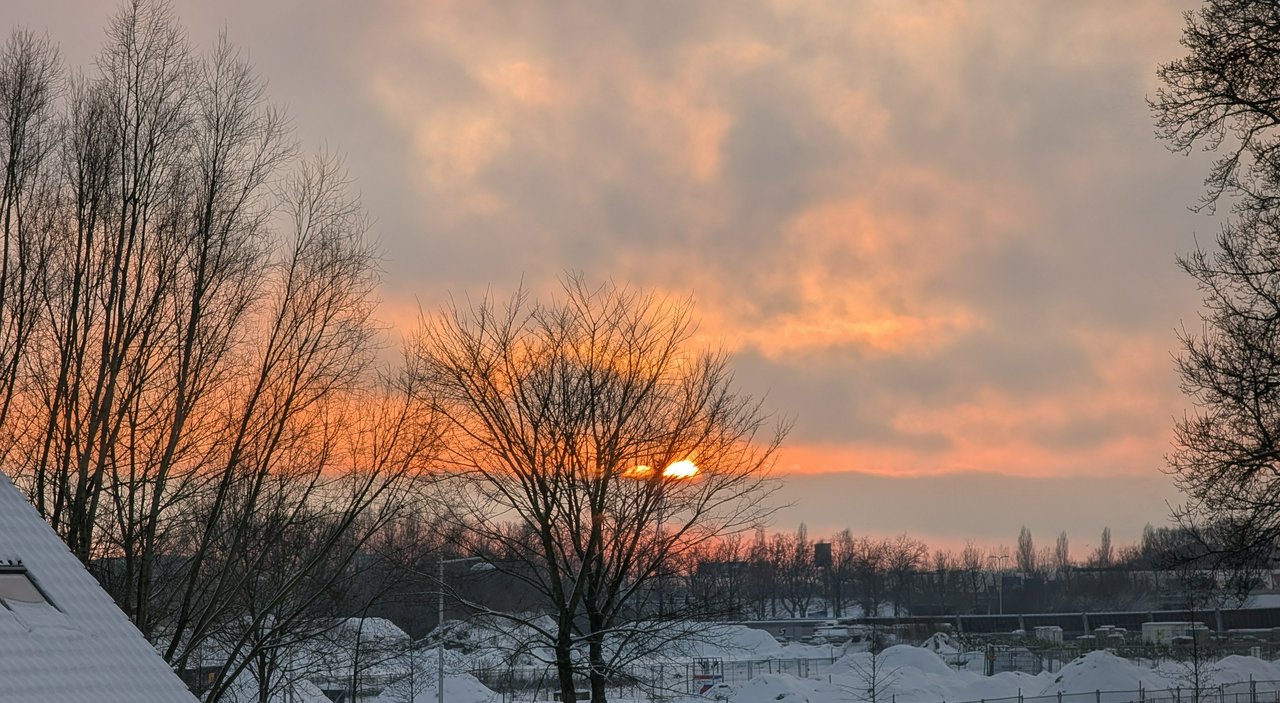 Dark orange sunset, partly clouded, snow covered roofs and fields