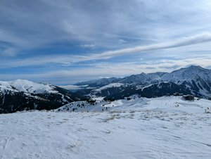 Some blue sky, white fluffy clouds and snow covered mountains in each direction.