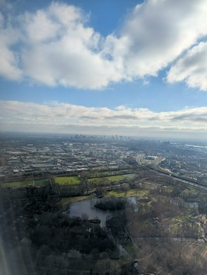 Looking out an airplane window, the skyline of Rotterdam in the distance, with some buildings and a park in the foreground.