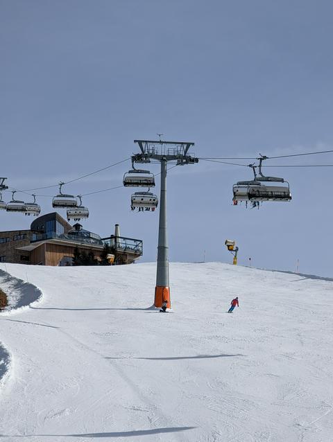 Two skiers, a slope, a ski lift and a restaurant in the background.