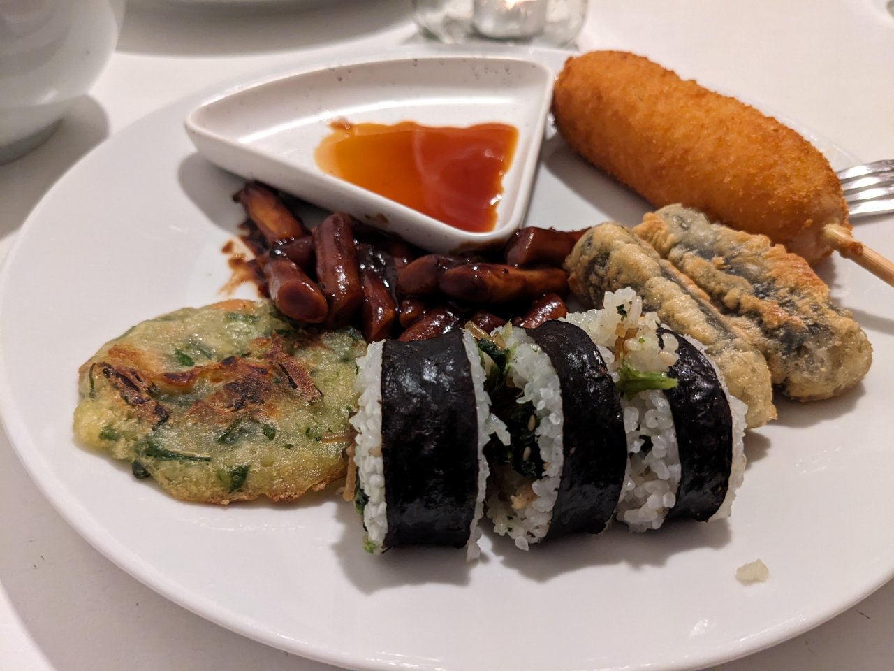 A plate of Korean food: Tteokbokki, corn-dog, gimbap, yachaejeon and gimmari